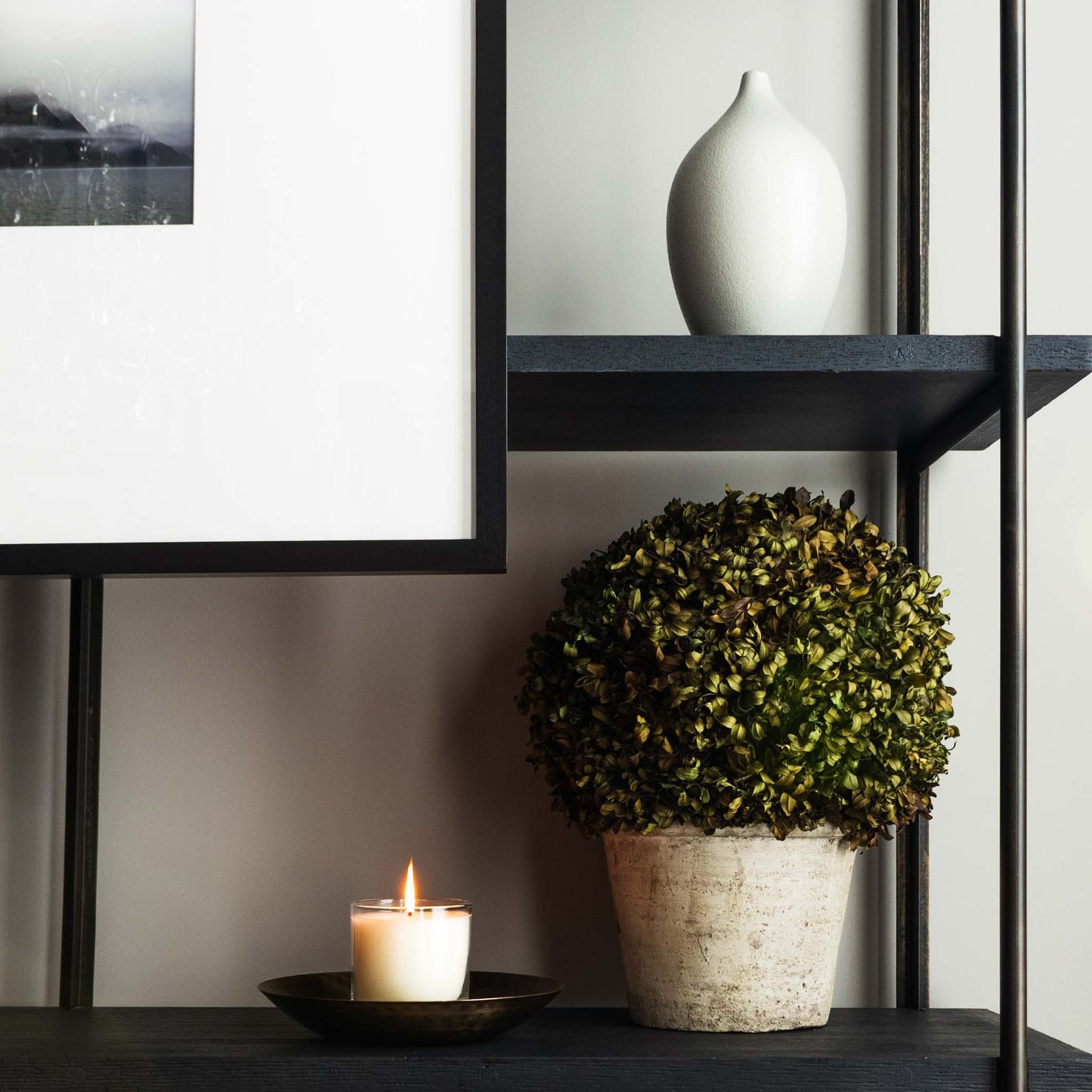 Luxury scented soy wax blend candle on hammered antique brass tray with black and white artwork and potted boxwood.