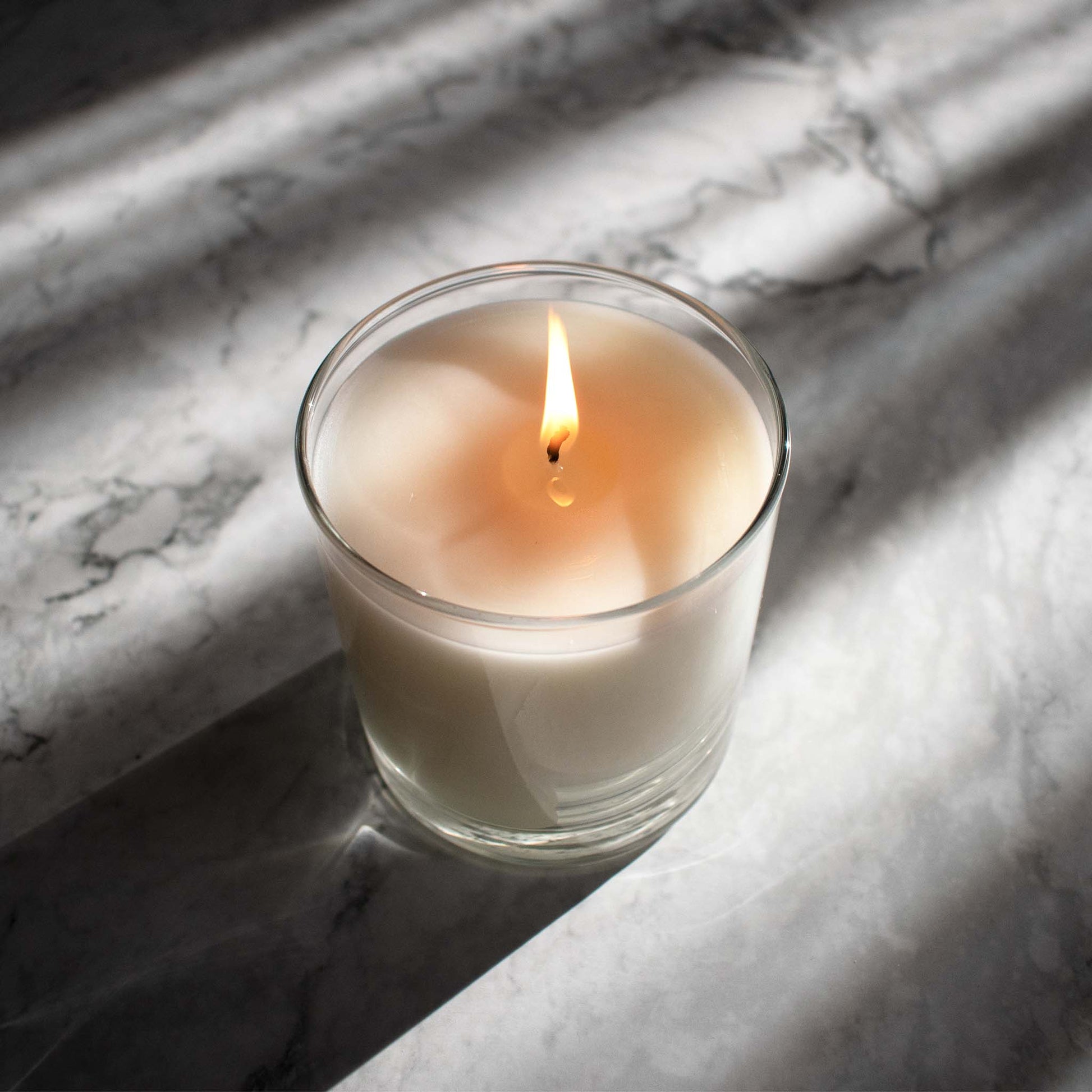 Luxury scented soy wax blend burning candle on marble table with sunrays.