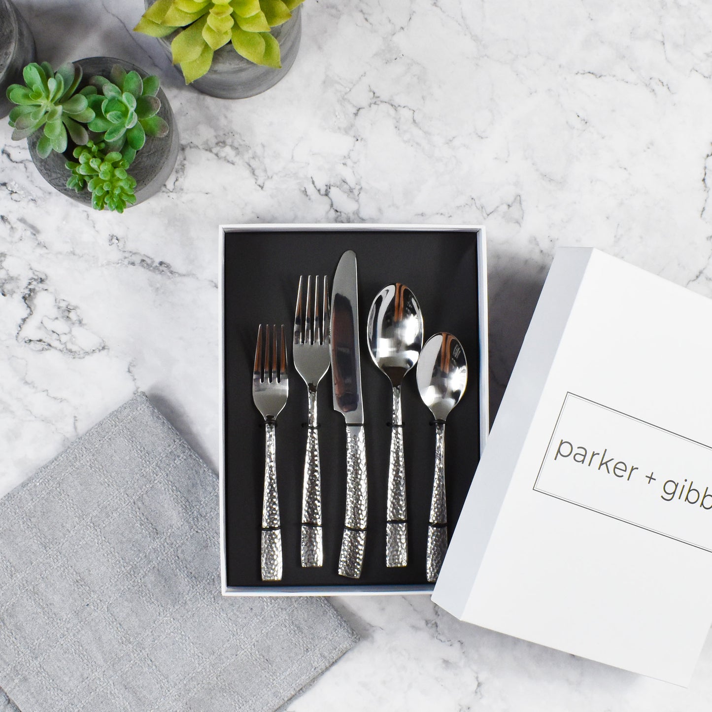 Polished silver hammered flatware  in custom box on marble countertop with succulents in concrete planters.