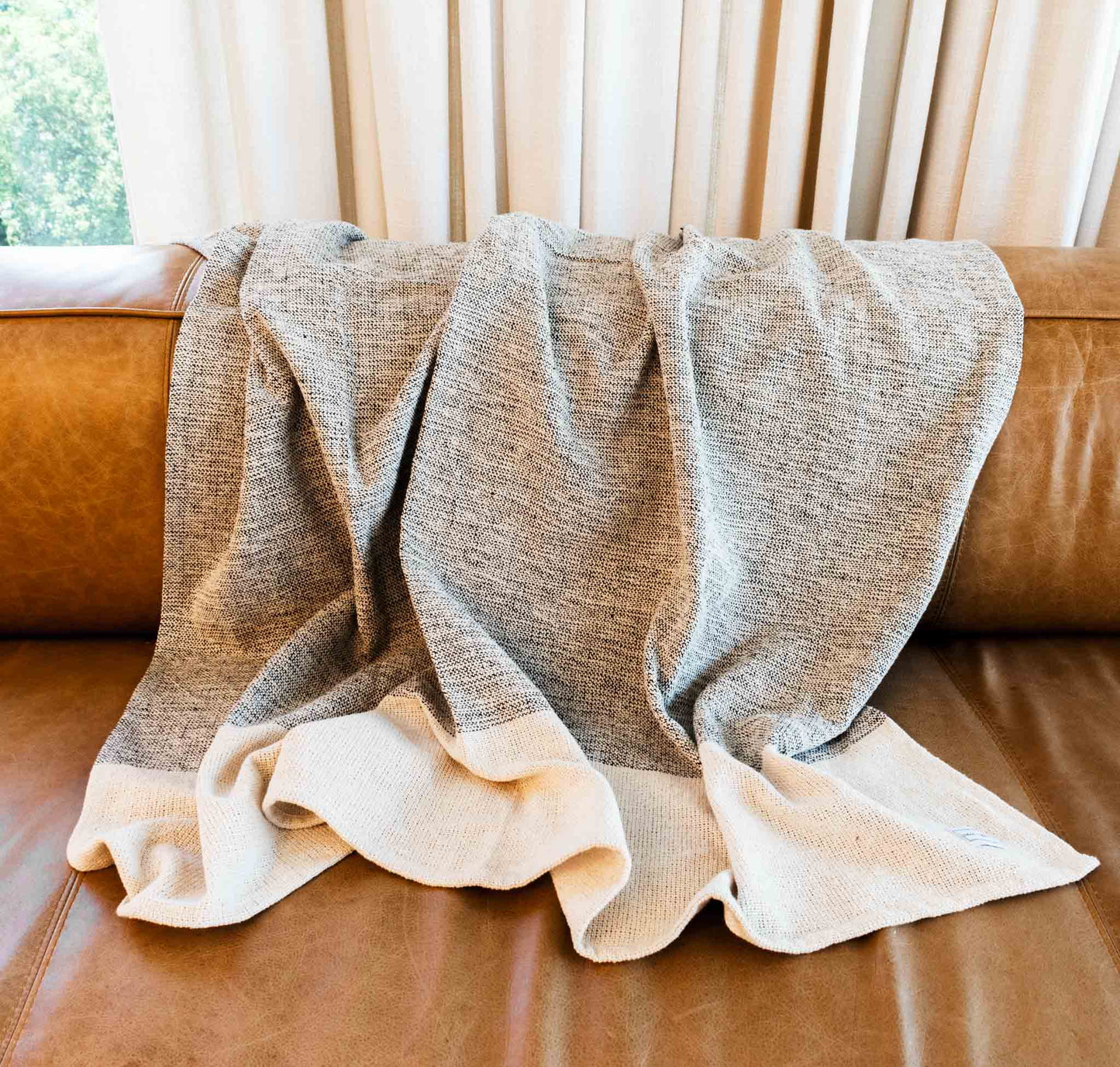 Cotton throw blanket with black and sand center block and sand border on leather sofa.