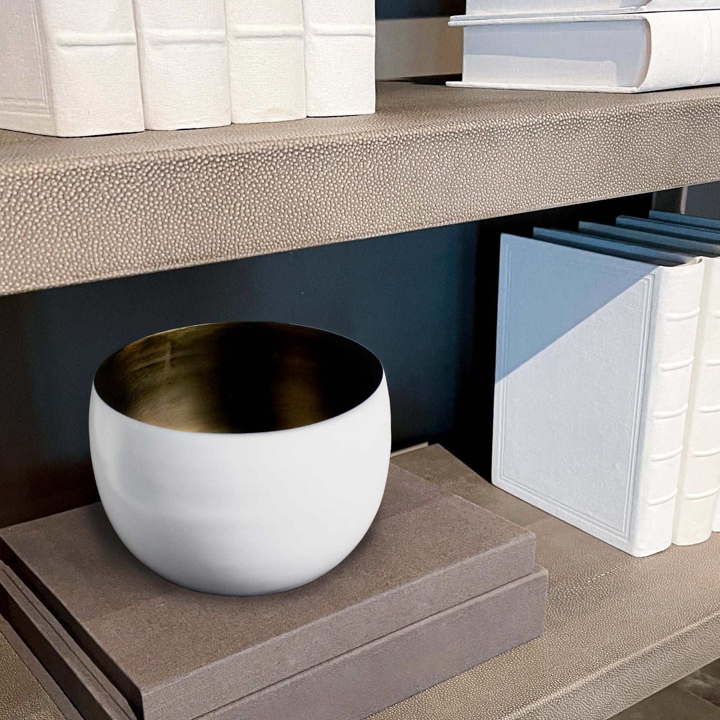 Decorative white bowl with antique brass finish interior on stack of books.