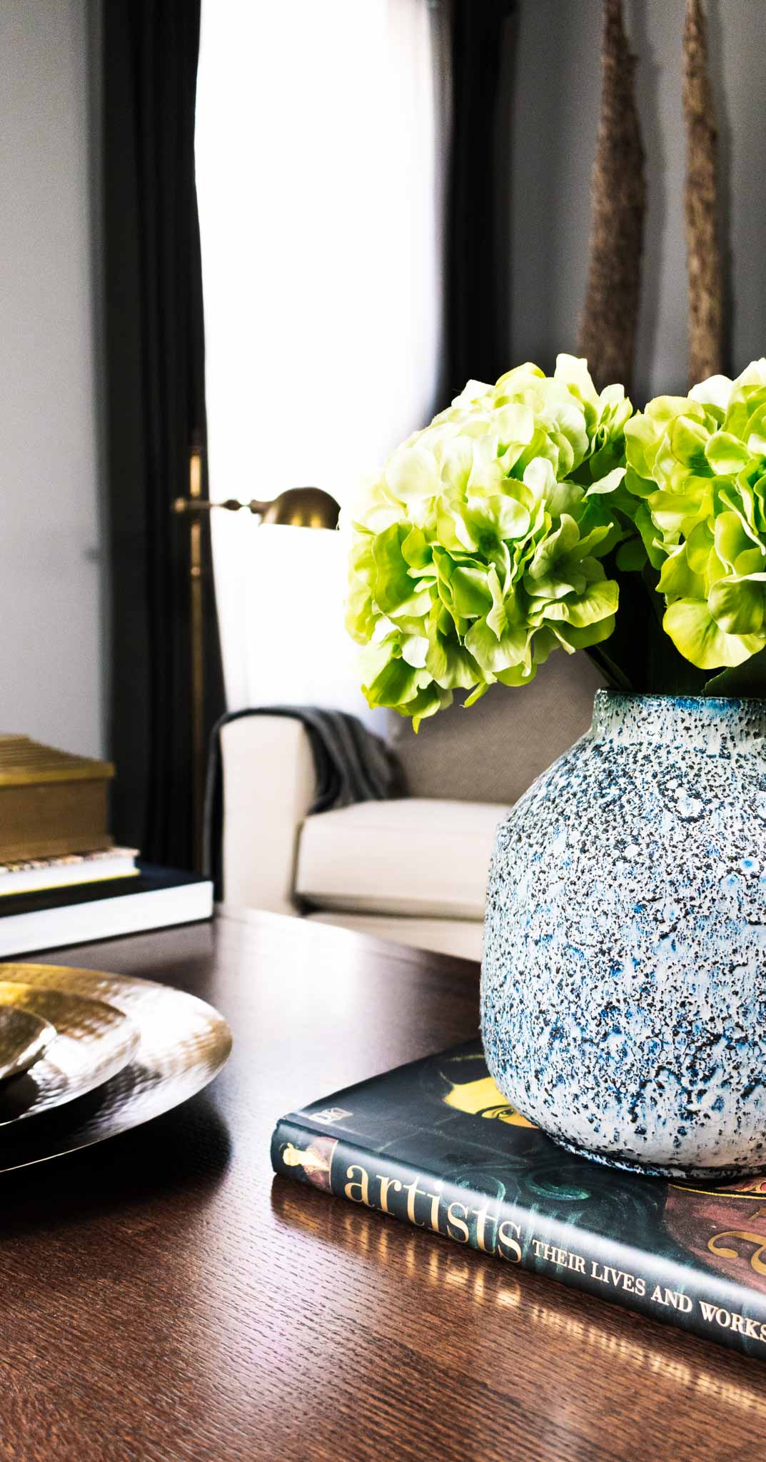 Handcrafted ceramic vase with rough textured surface with white, brown, and blue glazing in living room styled with hydrangeas.