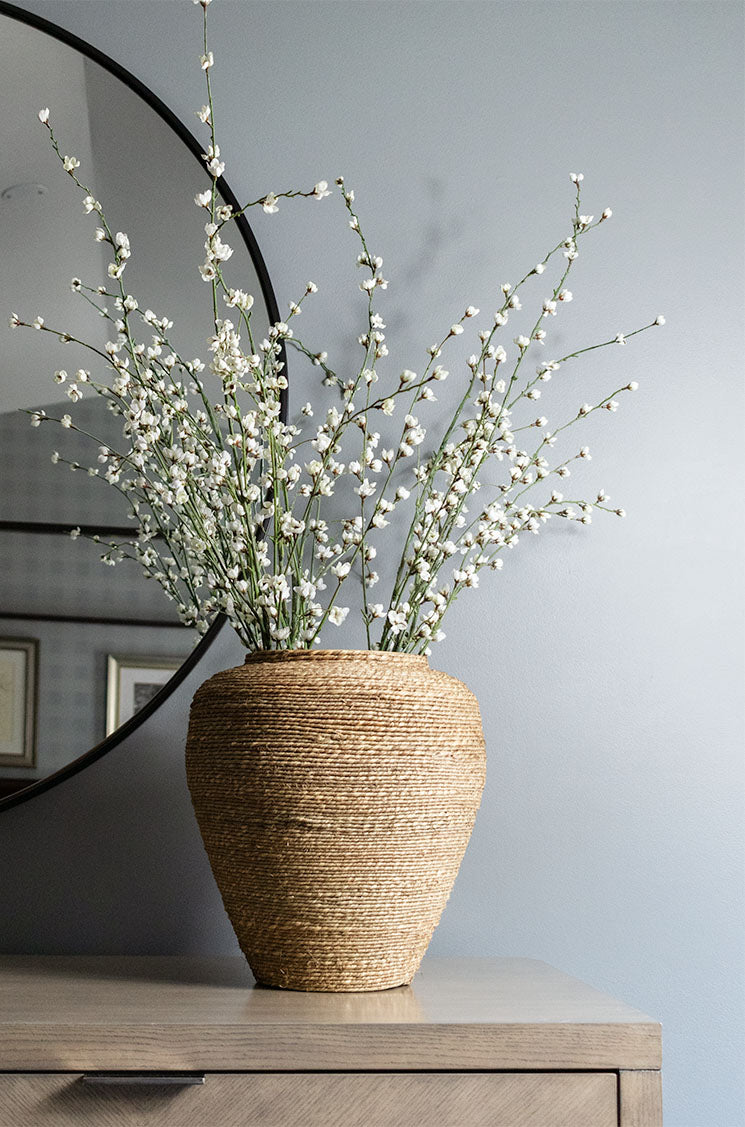 Handmade natural seagrass vessel with cherry blossom branches on dresser.