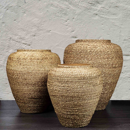 Handmade natural seagrass metal vessels on wood surface with textured background.