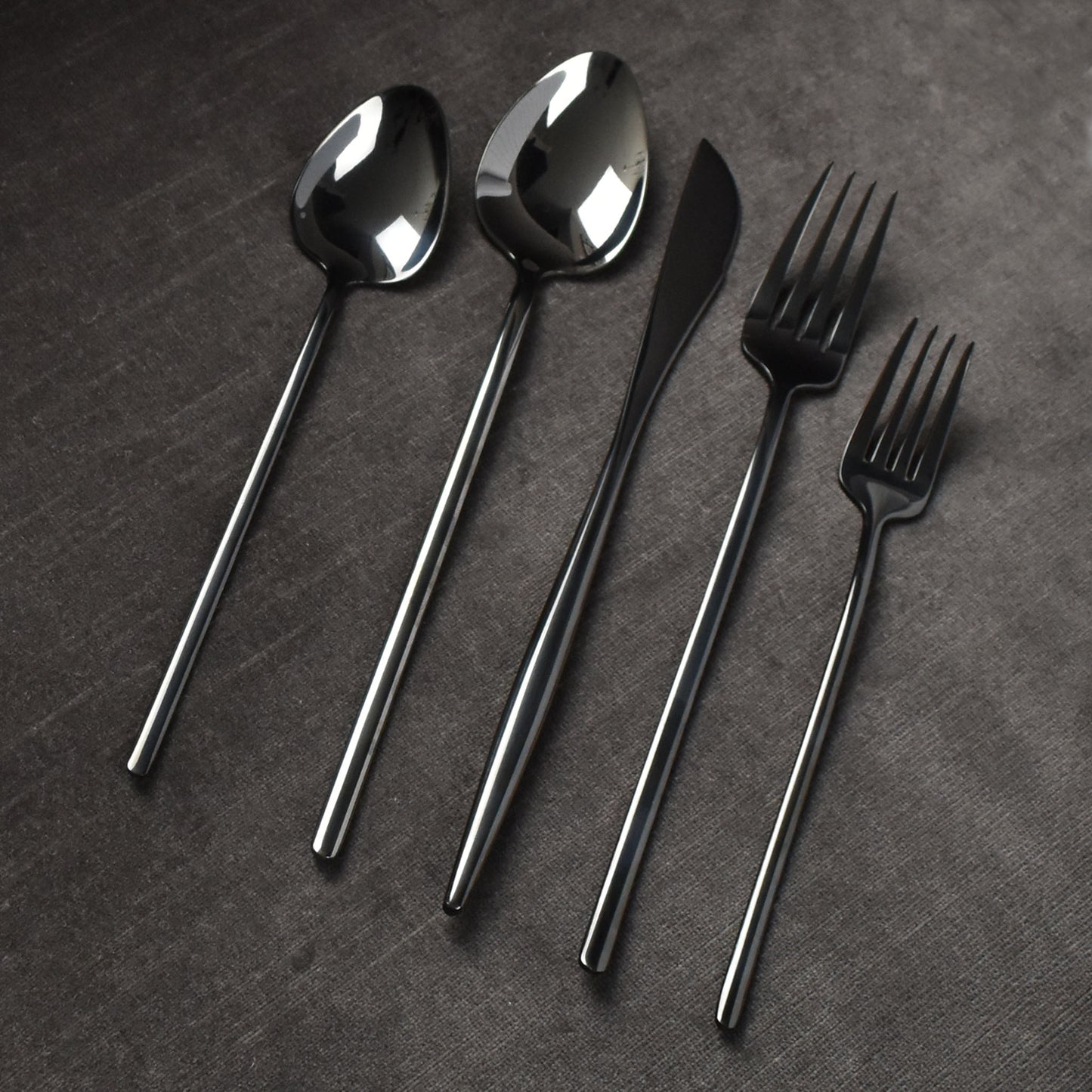 Mirrored polished black flatware on dark grey background.