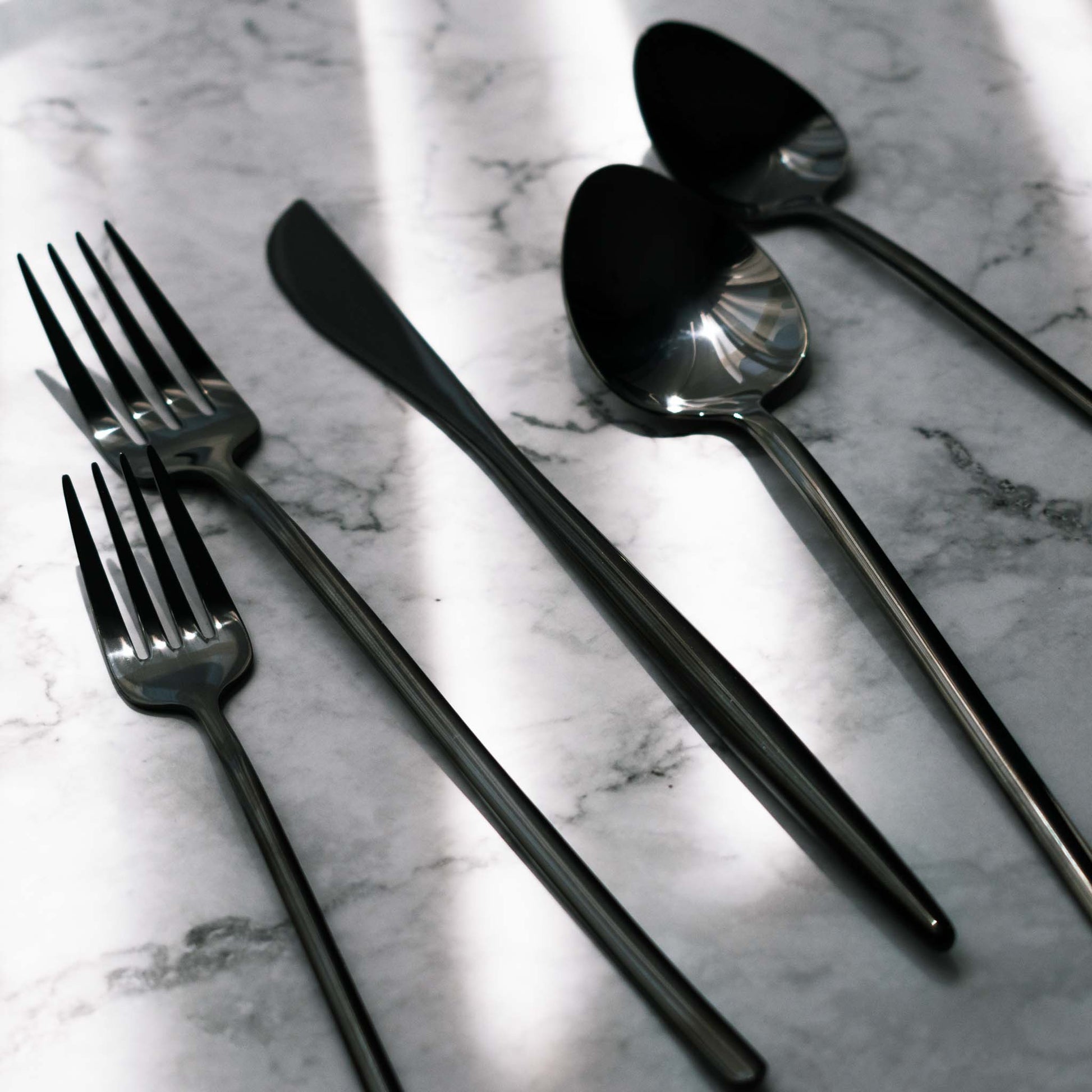 Shiny polished contemporary black finish flatware set on marble table.