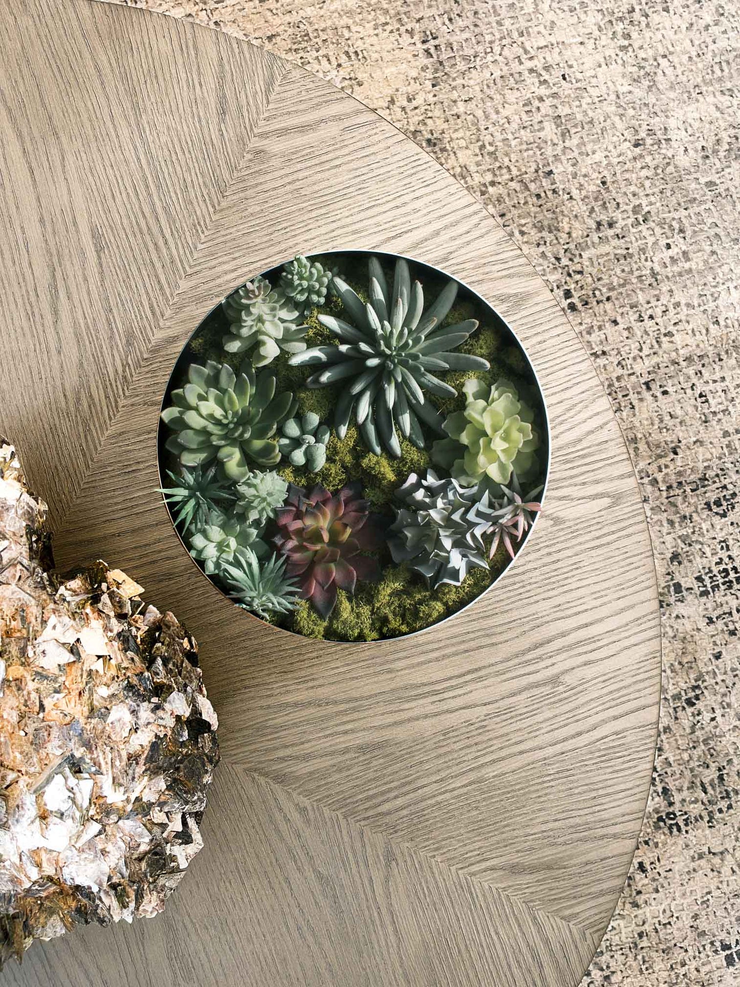 Large painted white decorative bowl with antique brass finish interior filled with succulents on table with geode object.