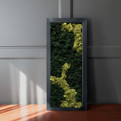 Matte black metal centerpiece tray filled with moss leaning against gray paneled wall.