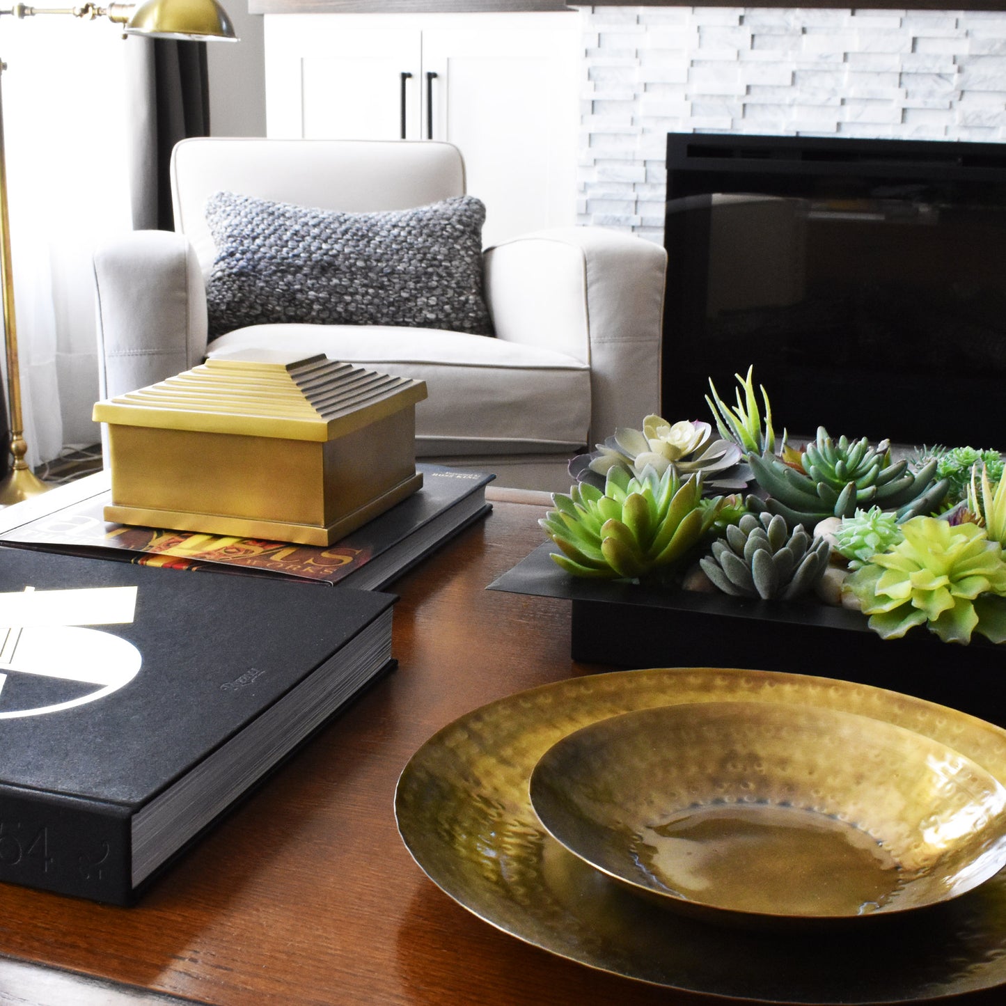Nested antique finished round brass trays, brass pyramid box, succulents in black tray, in living room.