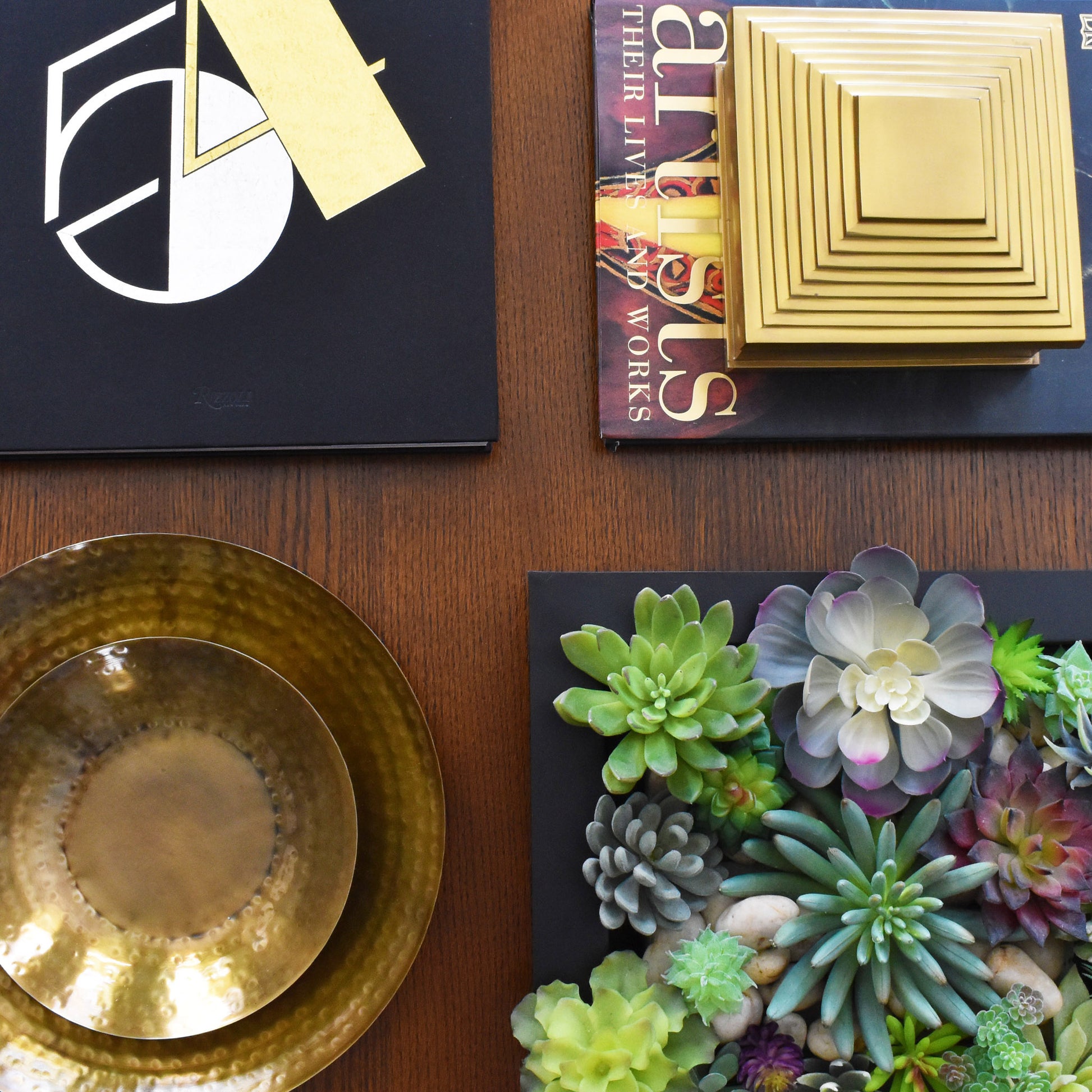 Nested antique brass finish trays, black metal tray with succulents, Studio 54 book, and brass pyramid box on oak coffee table.