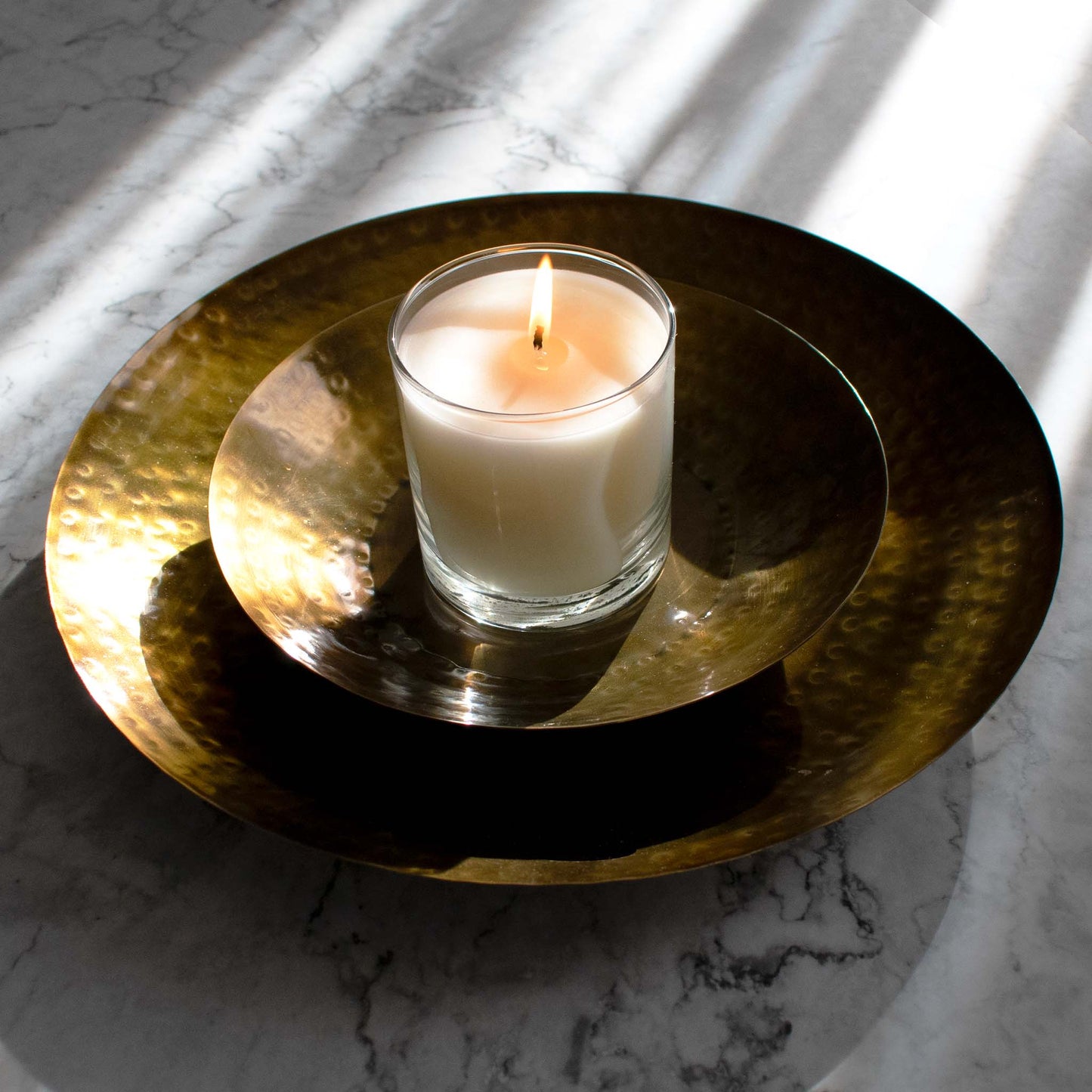 Nested antique finished round brass trays, with burning candle, on marble table.