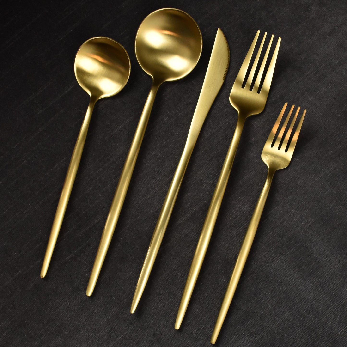 Matte brushed gold flatware on dark grey background.