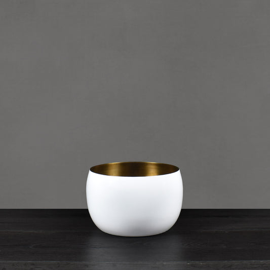 White enamel painted vessel with antiqued brass interior finish on dark wood floor with gray background.