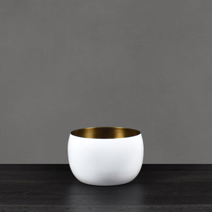 White enamel painted vessel with antiqued brass interior finish on dark wood floor with gray background.