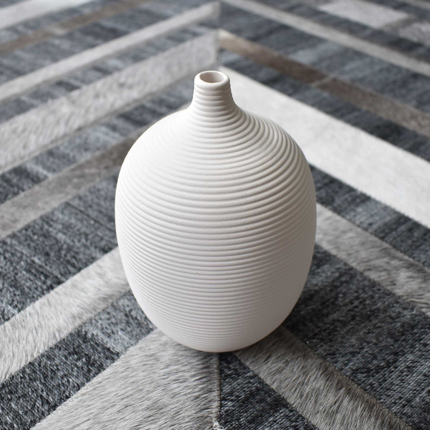 White ceramic ribbed decorative vase on chevron cowhide rug.
