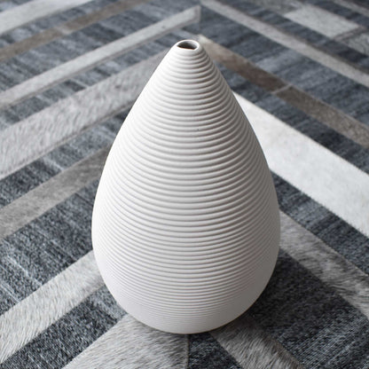 White ceramic ribbed conical vase on chevron cowhide rug.
