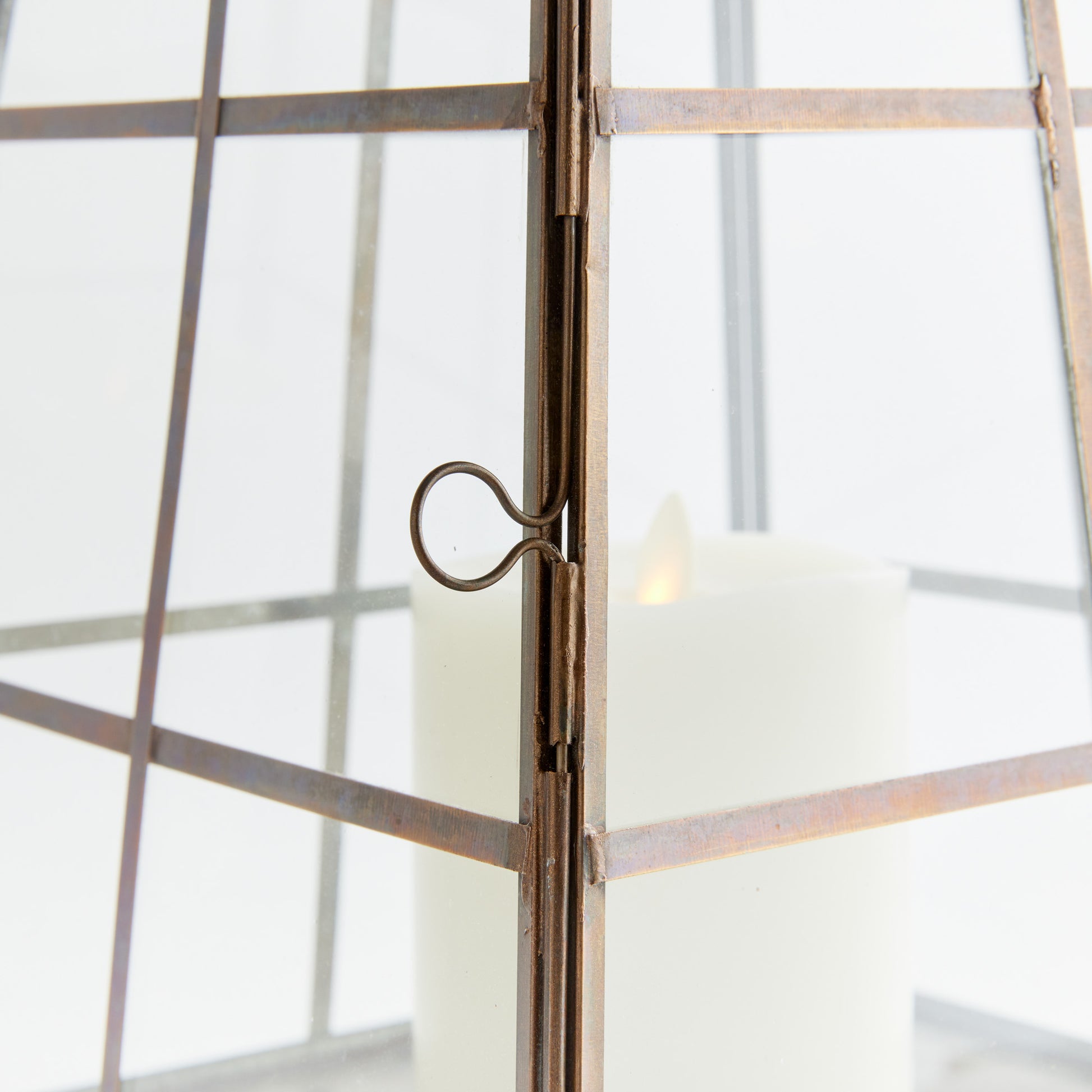 Antique brass metal lantern, closeup view of lantern door, with light gray background.