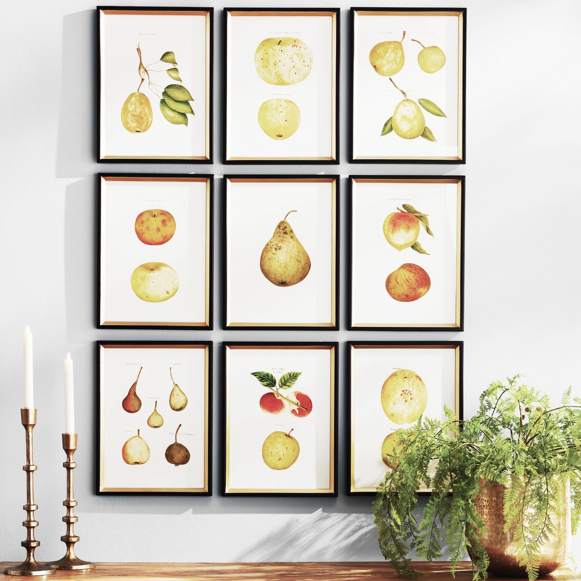 Assorted fruits gallery wall art set stylized over top of wood console table with taper candleholders and plant.