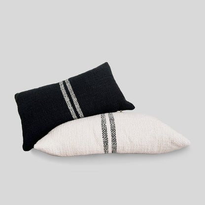 Black double striped lumbar pillow and cream double striped lumbar pillow with gray background.