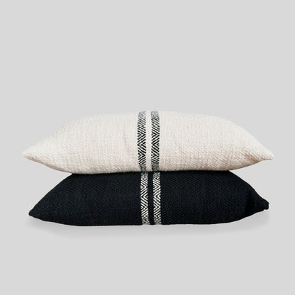 Black double striped lumbar pillow and cream double striped lumbar pillow stacked on top of each other with gray background.