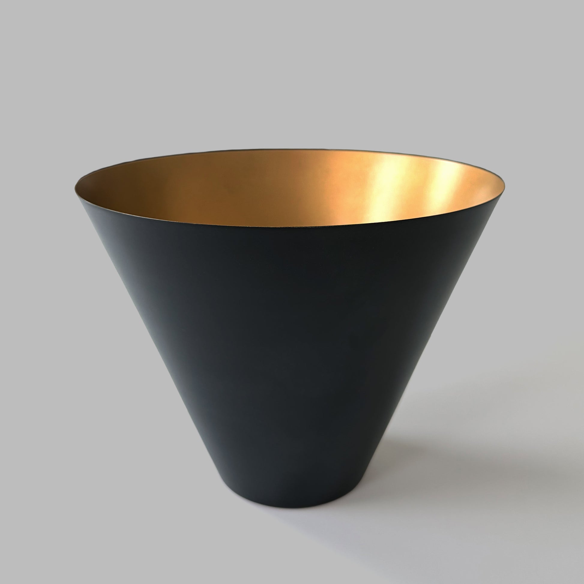 Large black and gold decorative metal bowl on gray background.