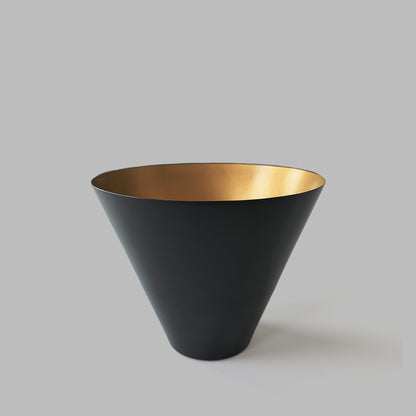 Medium black and gold decorative metal bowl on gray background.