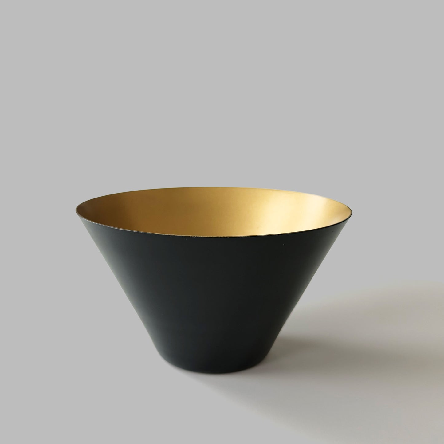 Small black and gold decorative metal bowl on gray background.