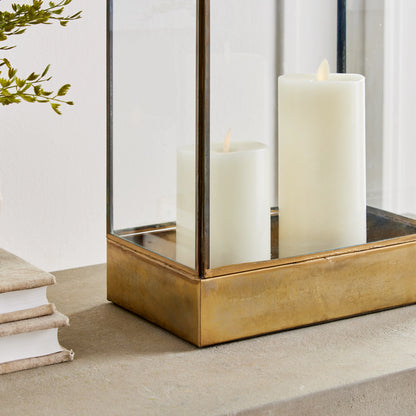 Brass hurricane candle holder with flameless candles on stylized table.