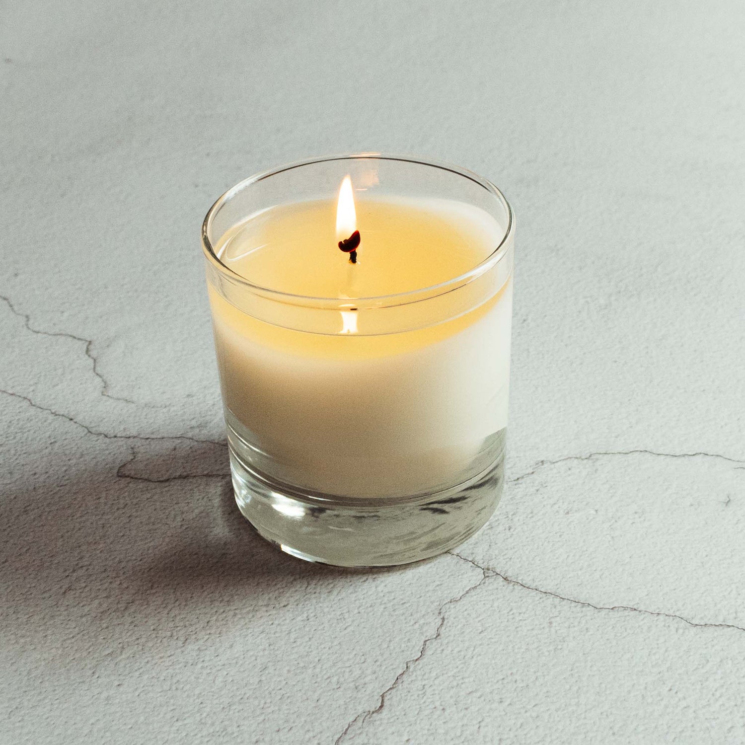Burning candle with white wax in clear jar on limestone counter.