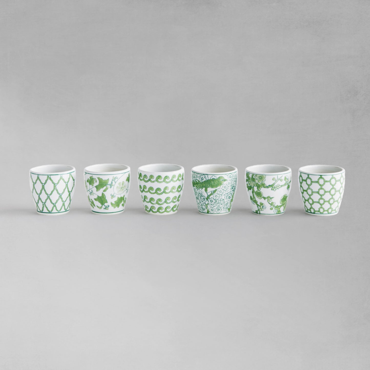 Set of 6 chinoiserie green and white porcelain flower pots lined up in a row with gray background.