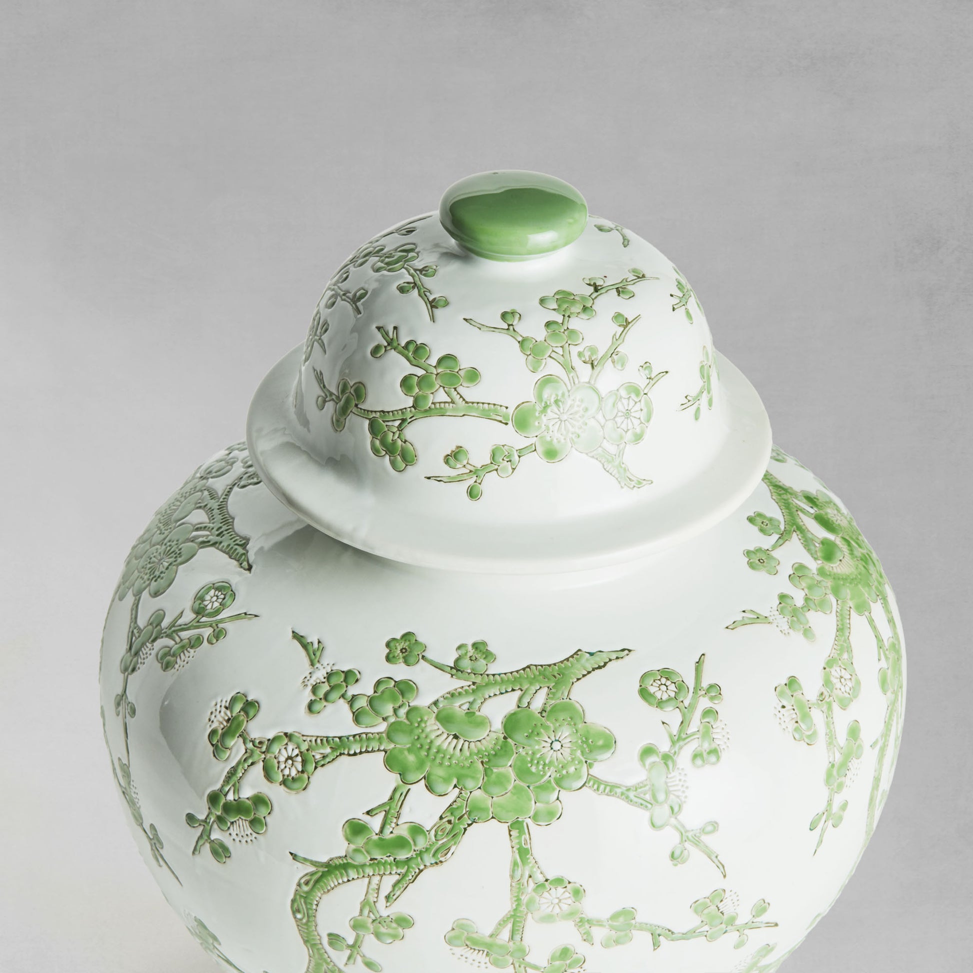 Chinoiserie green and white porcelain ginger jar, closeup view of lid with gray background.