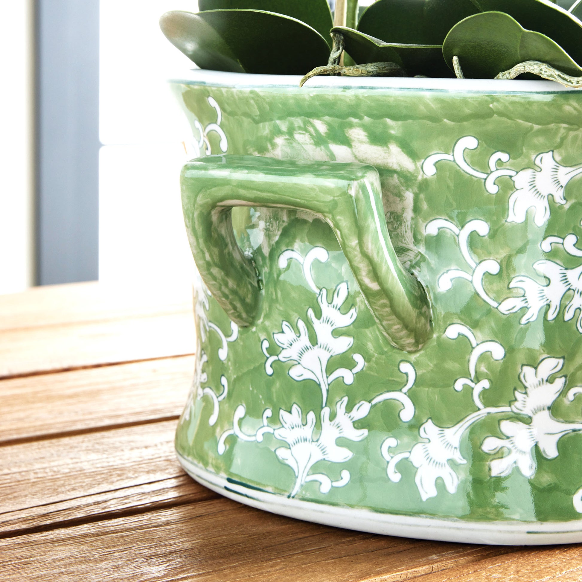 Chinoiserie green and white porcelain planter, closeup view of handle, stylized on wood table.