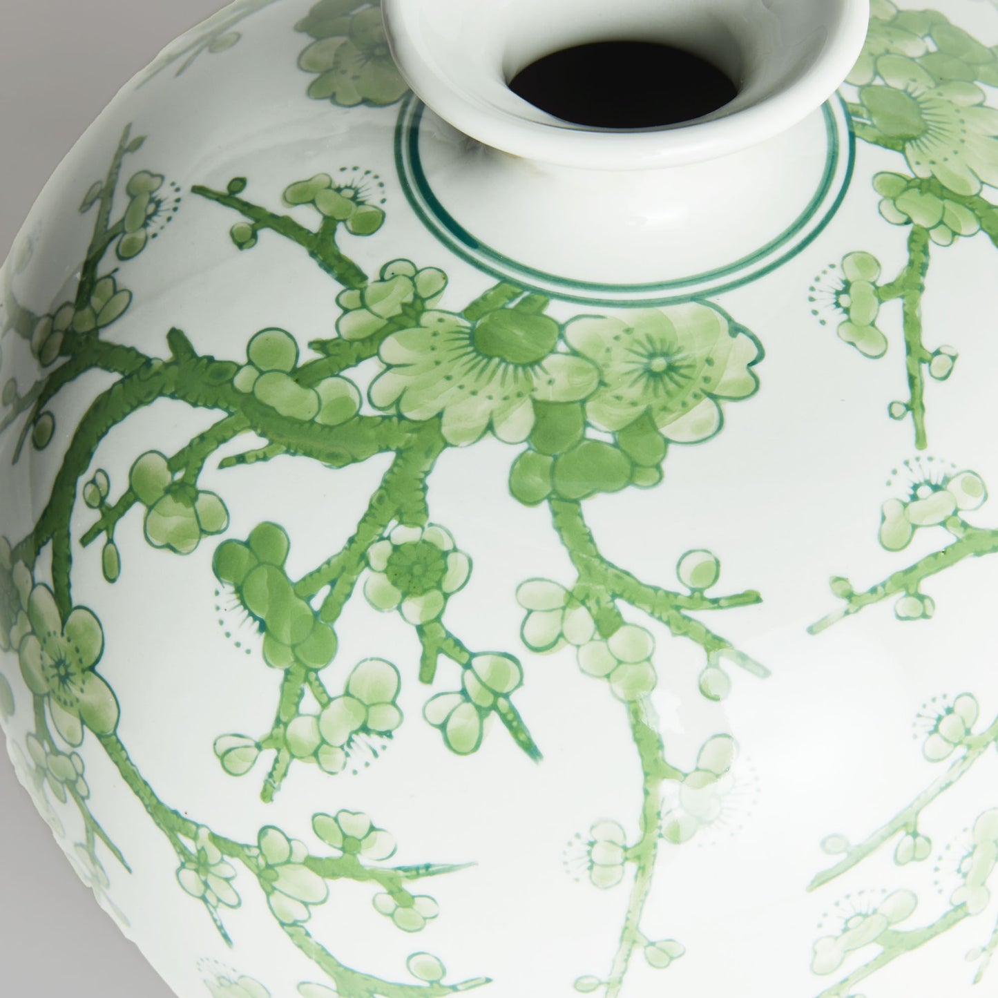 Chinoiserie green and white porcelain vase, closeup view of vase top with gray background.