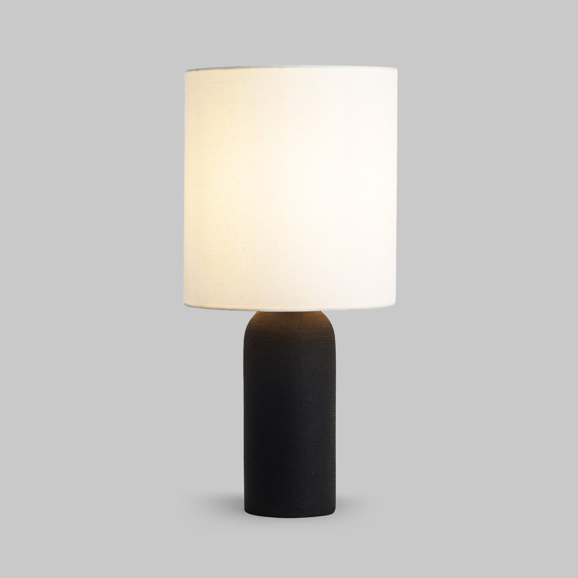 Contemporary black textured table lamp, illuminated.