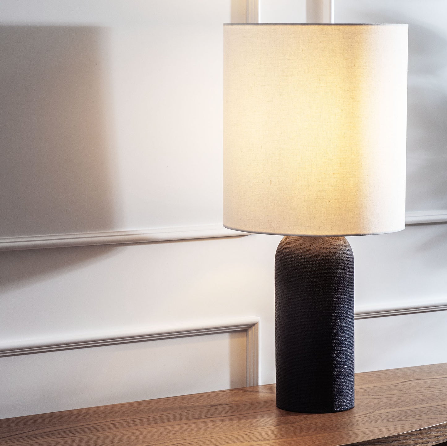 Contemporary black textured table lamp stylized and illuminated on console table.