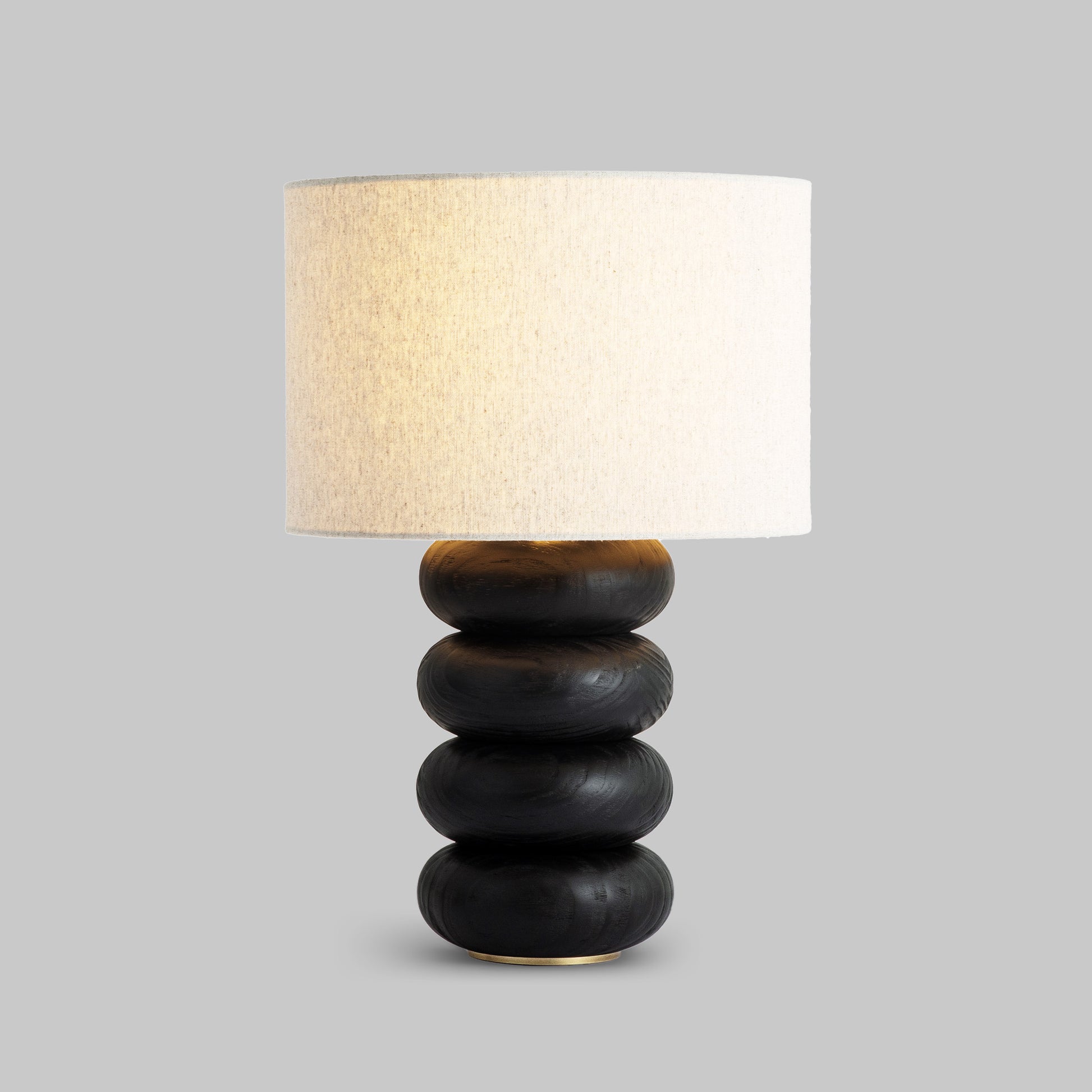 Contemporary stacked wood ring table lamp with black finish, illuminated.