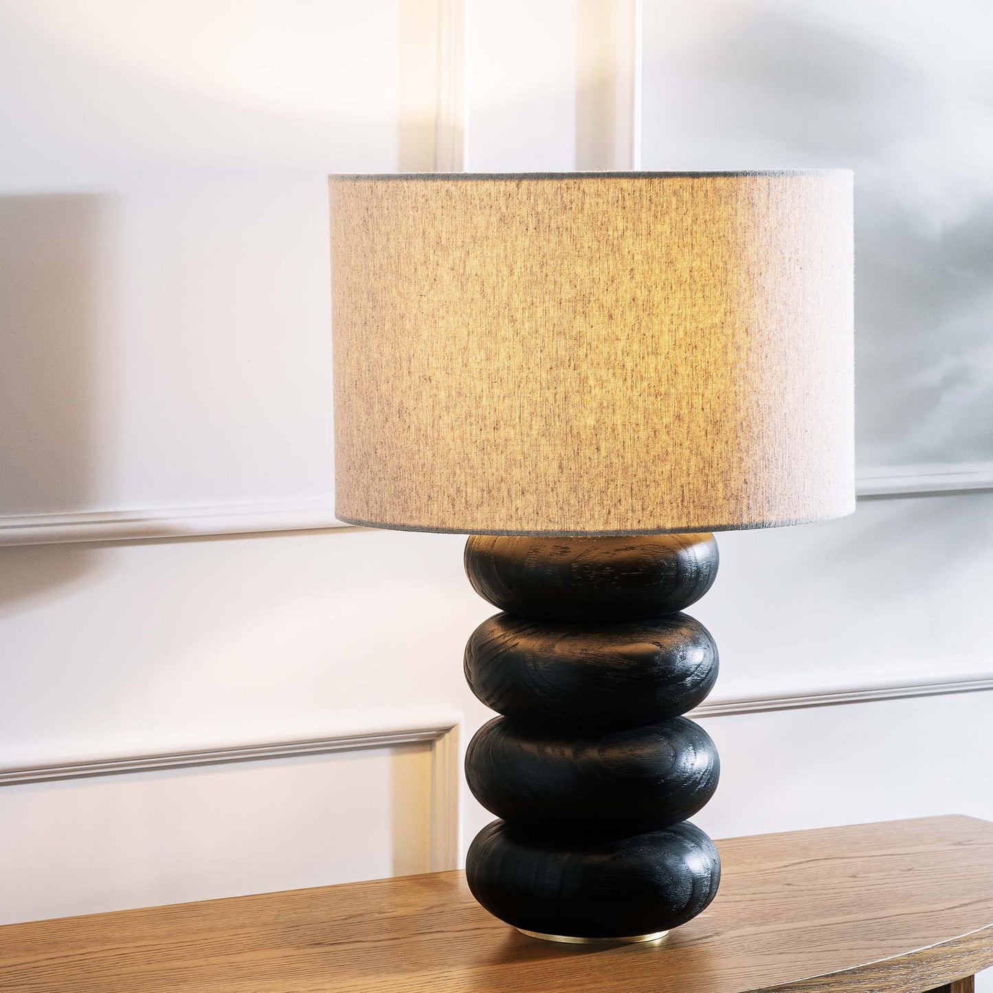 Contemporary stacked wood ring table lamp with black finish, stylized on console table.