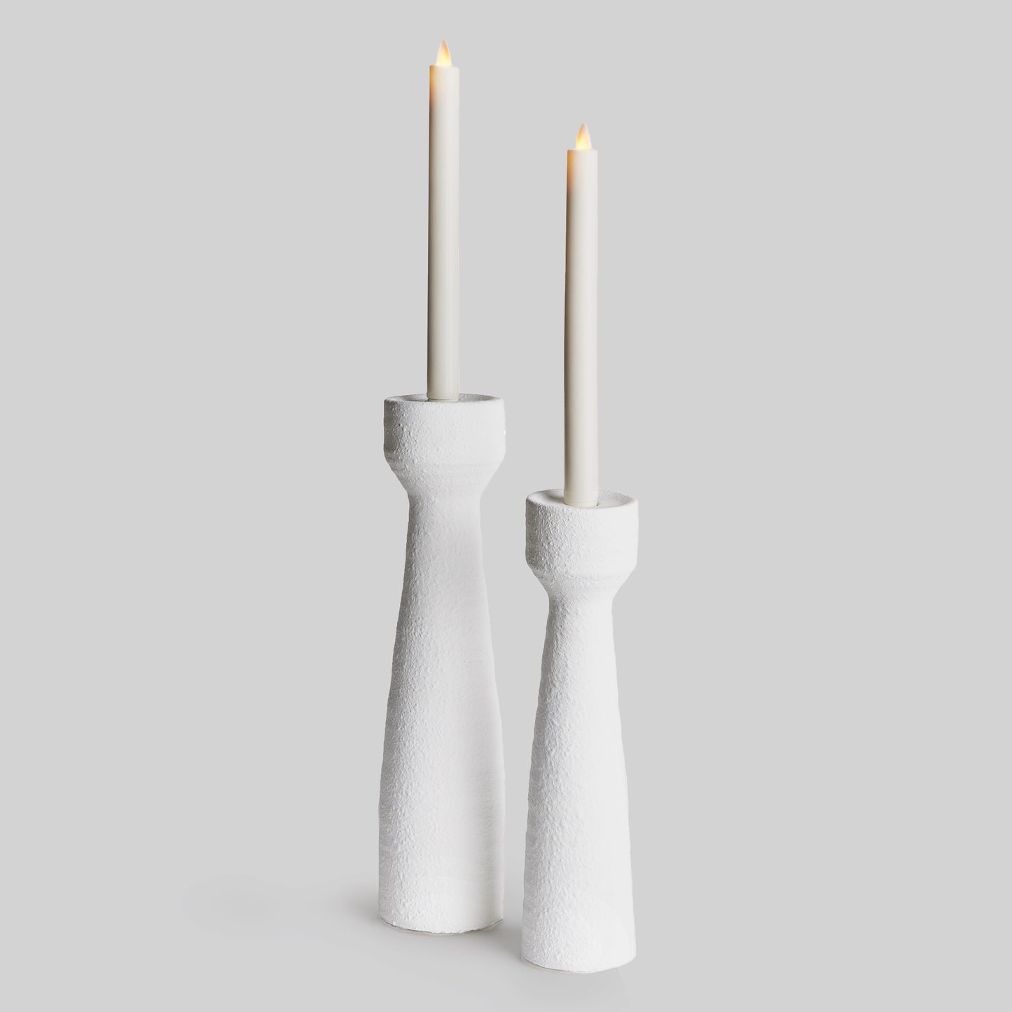 Closeup view of contemporary white terracotta candleholders, set of 2, with LED candles and gray background.