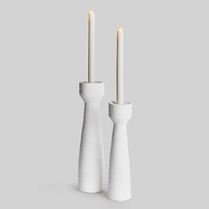 Closeup view of contemporary white terracotta candleholders, set of 2, with LED candles and gray background.