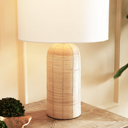 Cylindrical cane rattan table lamp, closeup view, stylized on console table.