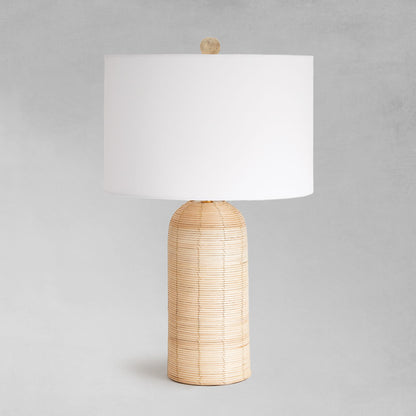 Cylindrical cane rattan table lamp with gray background.