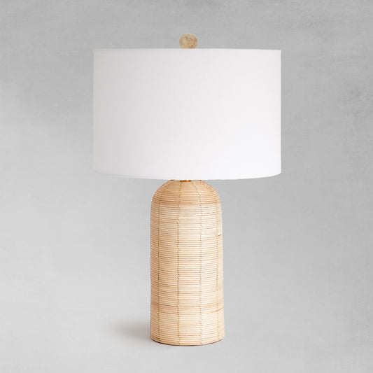 Cylindrical cane rattan table lamp with gray background.