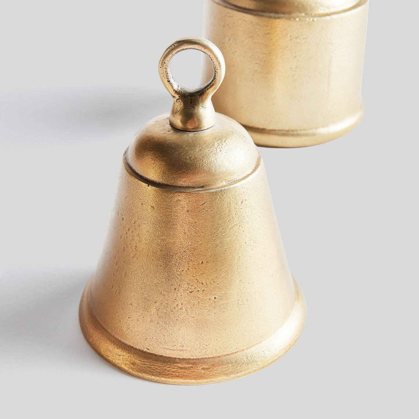 Decorative gold bells, set of two, top view, with gray background.