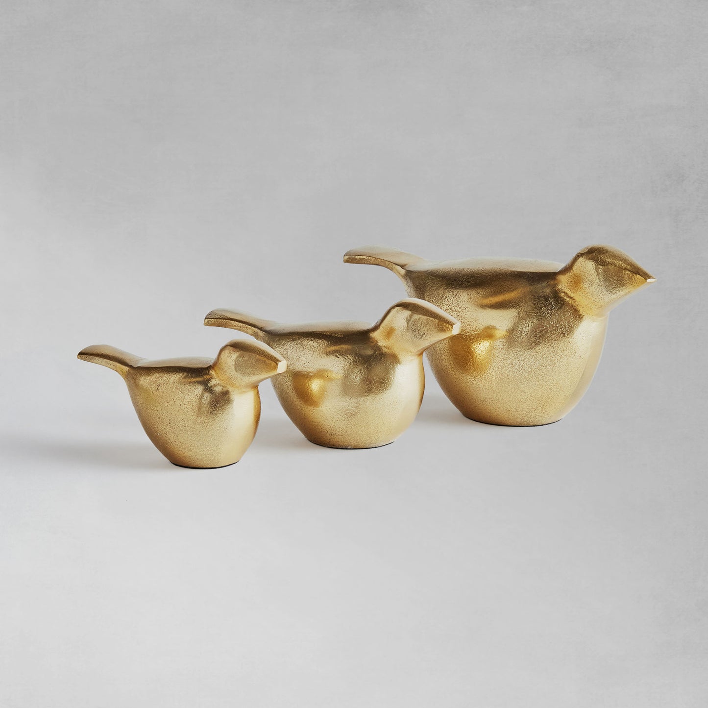 Decorative gold bird objects, set of 3, lined up, with gray background.