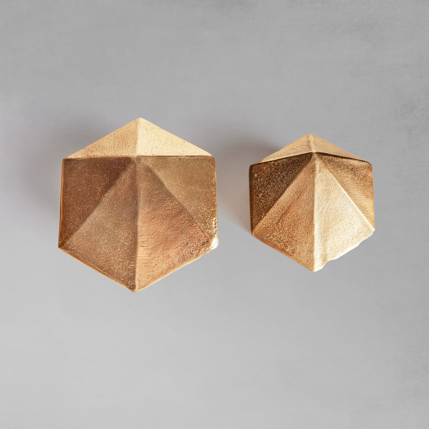 Decorative gold geometric lidded boxes, top view, with gray background.