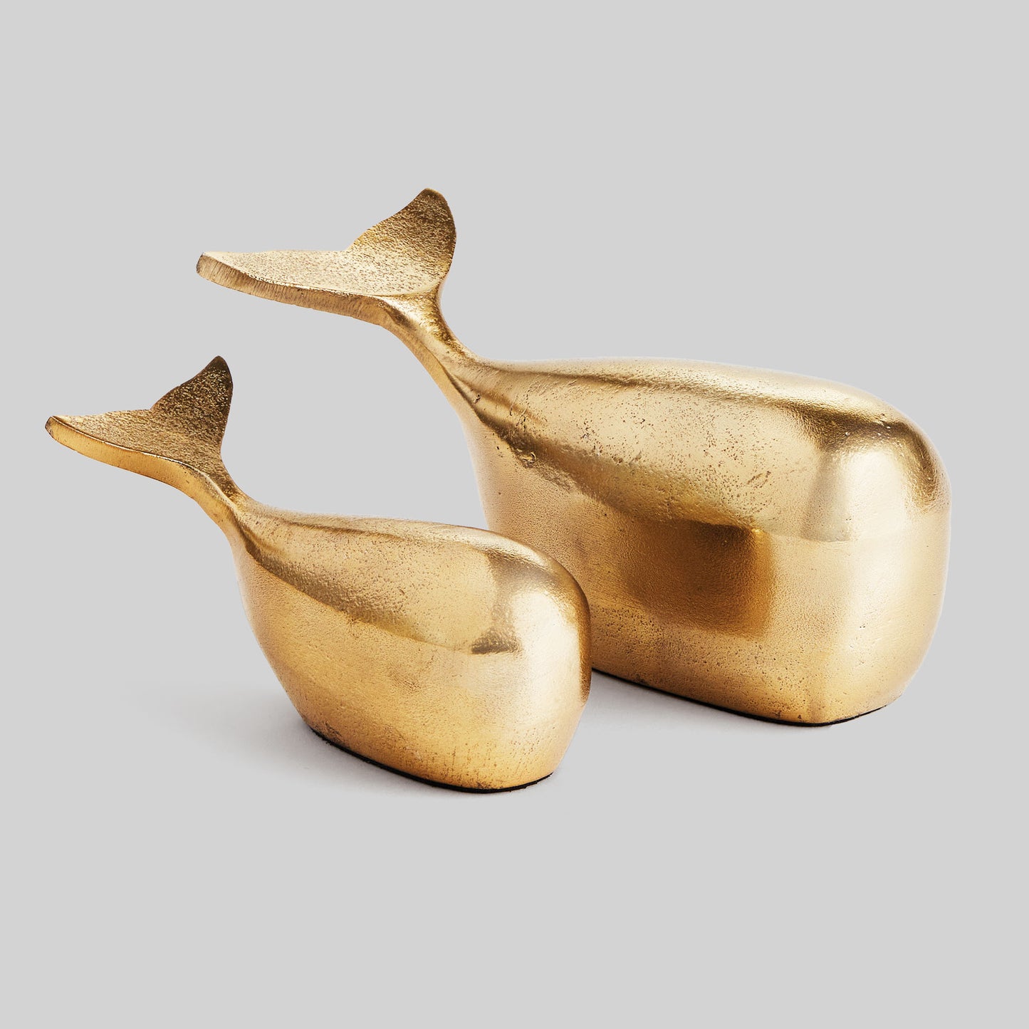 Decorative gold metal whale objects, set of 2, with gray background.