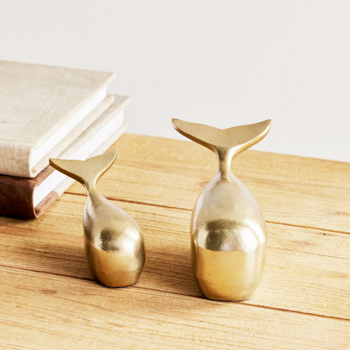 Decorative gold metal whale objects, set of 2, stylized on wood table.