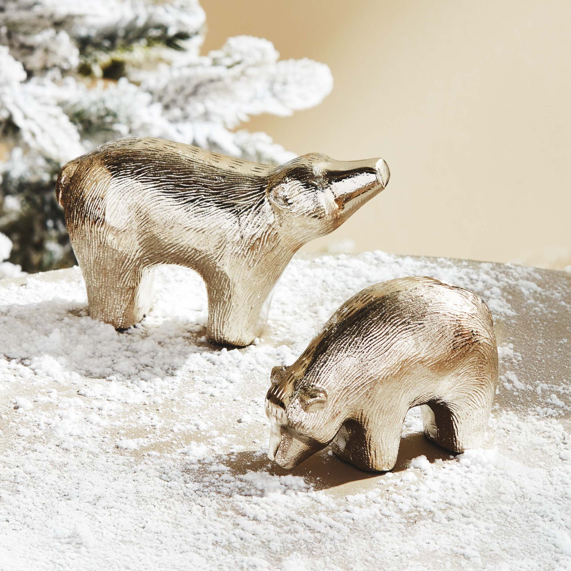 Decorative silver bears, set of two, on table with snow and Christmas tree in the background.