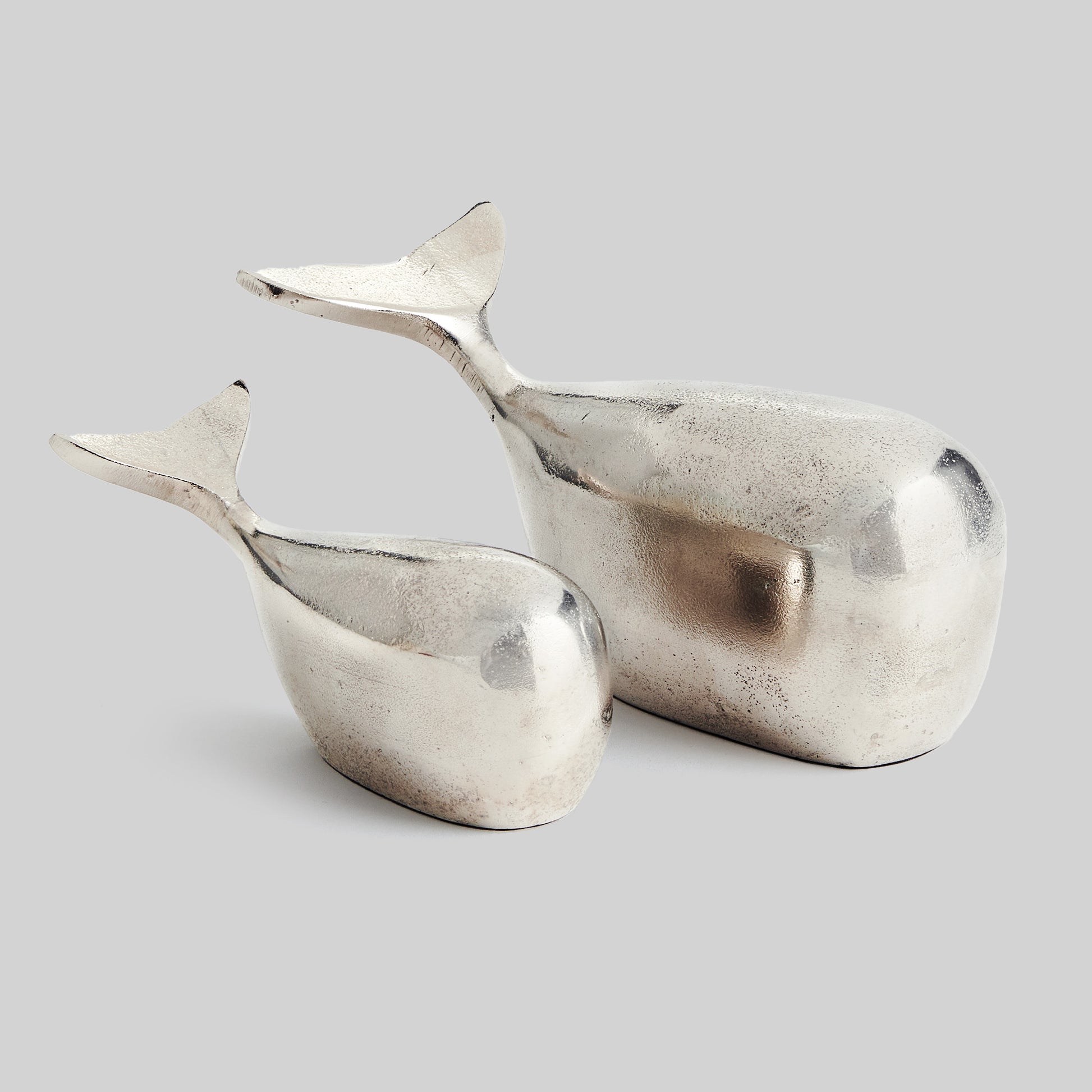 Decorative silver metal whale objects, set of 2, with gray background.