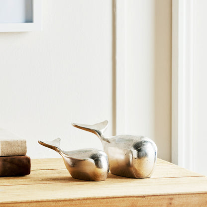 Decorative silver metal whale objects, set of 2, stylized on wood table.